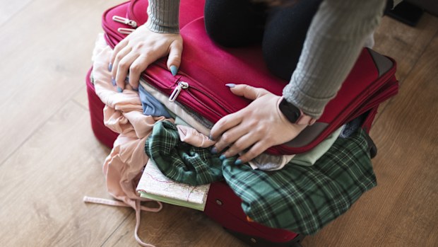 Unrecognisable woman struggling with closing the full suitcase.