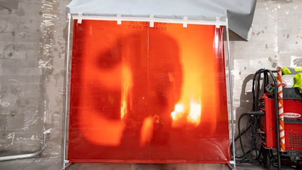 A welder stands behind a protective shield at the lowest level of the ITER cryostat base.
