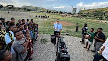 9News reporter Zac Bailey does a piece to camera as PNG locals watch on.