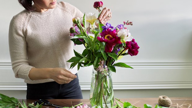 Mature woman at home with spring flowers. Female making bouquet, placing flowers in jug of water. Spring summer season, floristry, home decoration, natural beauty concept