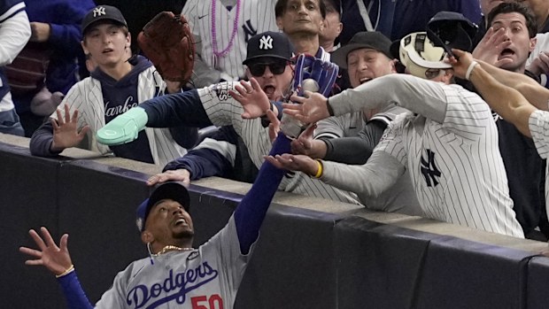 Fans interfere with a foul ball caught by Los Angeles Dodgers right fielder Mookie Betts during the first inning in Game 4 of the baseball World Series against the New York Yankees, Tuesday, Oct. 29, 2024, in New York. (AP Photo/Ashley Landis)