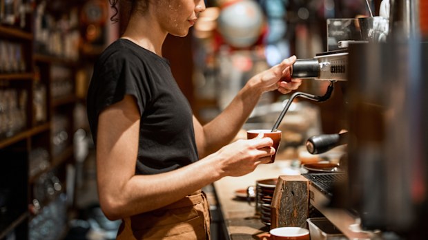 Aboriginal waitress in black attire operates professional espresso machine
