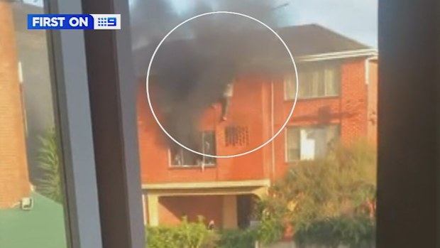 A man has been saved by his neighbours after they saw him hanging from the window of his burning apartment in Melbourne.