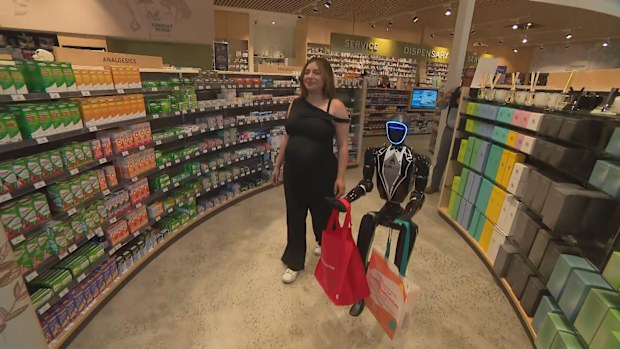 Woody, the humanoid AI assistant helping a woman carry shopping bags out of a store. 