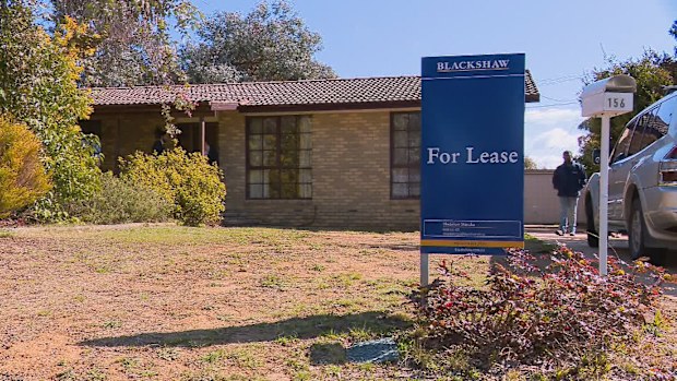 A blue "For Lease" sign out front of a brick house.