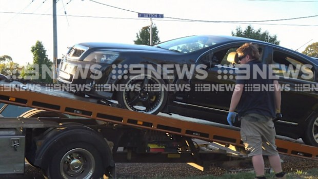 A tow truck driver watches as a black car is winched on to the back of a truck.