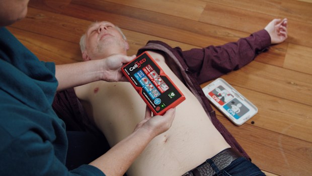 A man lies on the floor while someone sits above him holding a device