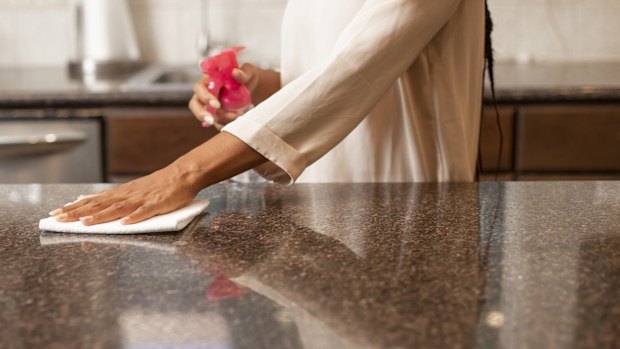 A woman cleaning and disinfecting kitchen bench, wiping surface