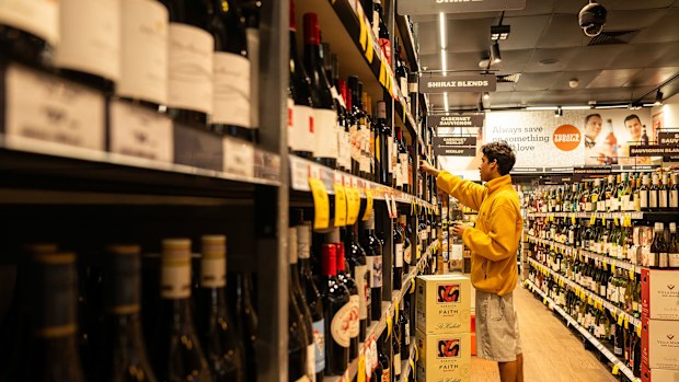 Someone selects a bottle of wine from a shelf in a bottle shop