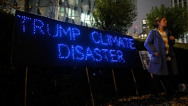 A woman stands beside a banner reading "Trump Climate Disaster" as a small group of demonstrators hold a protest against the new Trump Presidency 