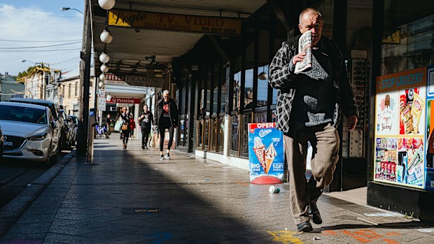 A man walks down the street past a row of shops