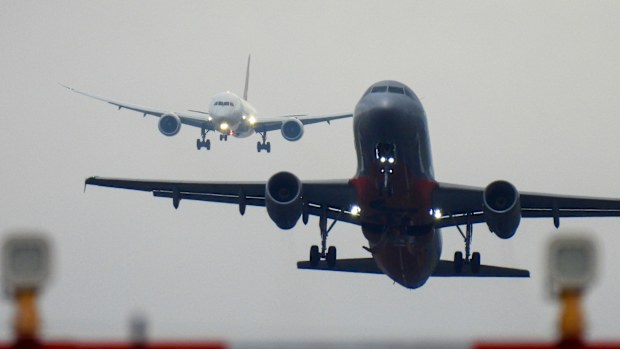 A Qantas Boeing B787-9 plane, registration VH-ZNL, coming into land from the north on the main runway of Sydney Kingsford-Smith Airport as flight QF28 from Santiago.  In the foreground is a Jetstar A320-232 plane taking off from the main runway and heading to the Gold Coast as flight JQ422.  In the near foreground are landing lights and their structures. This image was taken near Nigel Love Bridge, Mascot on an overcast and rainy afternoon on 25 November 2023.