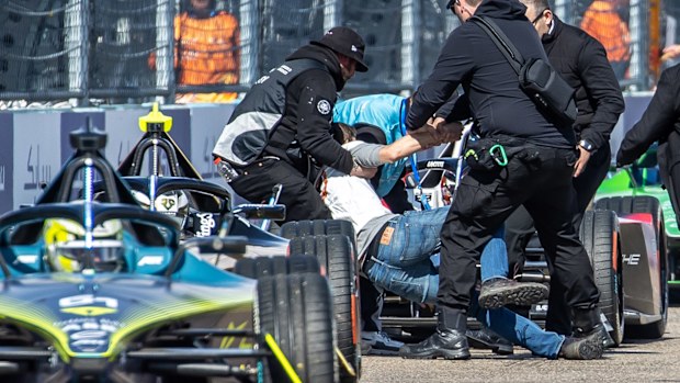 Security forces drag a last-generation climate activist off the track among the Formula E race cars ready to start. Photo: Andreas Gora/dpa (Photo by Andreas Gora/picture alliance via Getty Images)