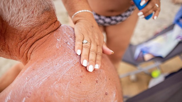 A thoughtful elderly woman applies sunscreen to her husband's arms and shoulders to shield his skin.