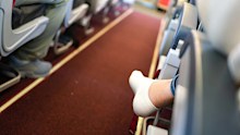 Action of an airplane passenger is crossing legged sitting at the economy class, with narrow corridor as blur background. People in transportation action, close-up and selective focus at heel part.