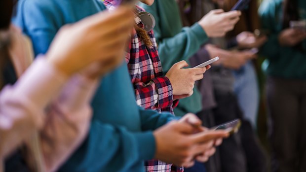 Close-up group of teenagers using mobile phones in school corridor