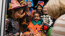 Taken from inside a residential house, two families wearing fancy dress, out trick or treating in North East England during halloween. The children are taking sweets off a plate that an unrecognisable woman is holding.