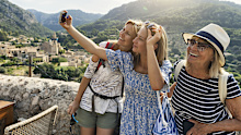 Multi generation family sightseeing beautiful town of Valldemossa. Sunny summer day in Majorca, Spain. Teenage girl, mother and grandmother are taking selfies. Behind them there is a magnificent view of the town of Valldemossa and the surrounding mountains - Serra de Tramuntana. Canon R5