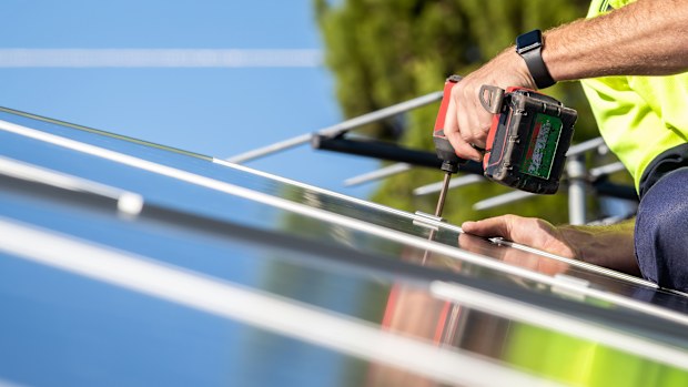 Unidentified electrician performing installation of solar panel on house roof using cordless screwdriver