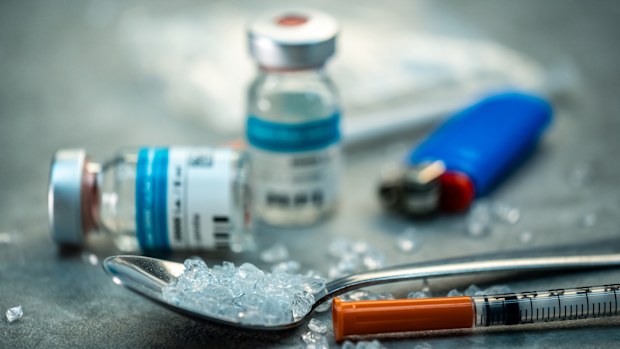 Close-up of methamphetamine crystals on a spoon, surrounded by a syringe, lighter, and vials, depicting drug use and addiction.