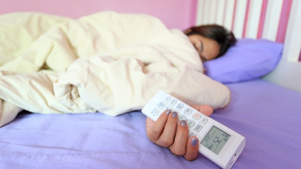 Young woman hand hold remote air conditioner and sleeping in the bedroom at home