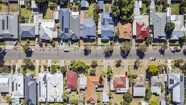 Aerial view directly above established houses in older Adelaide southern suburb: looking down on front & back yards some landscaped, one with construction work. Yellow & red topped wheeled garbage (rubbish) bins are parked on kerbside awaiting collection. Powerlines run down the street for the houses. Cars parked on the street and in private properties.