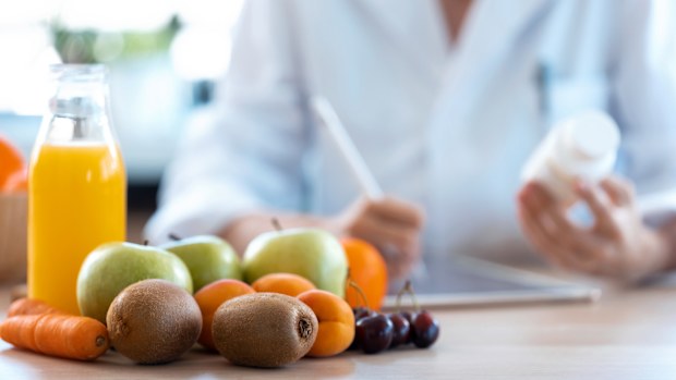 Close-up of woman nutritionist doctor writes the medical prescription for a correct diet on a desk with fruits, pills and supplements.