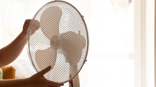 Man holding floor fan with hands at home in bedroom on hot day in summer