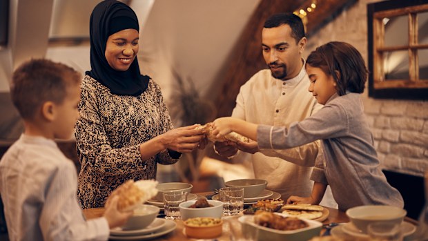 Happy Middle Eastern family sharing pita bread at dining table on Ramadan during iftar.