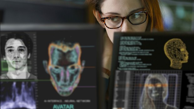 Stock photograph of a young, good looking, woman working in a dark office. She's surrounded by computer monitors depicting aspects of AI avatar & visual chatbot creation.