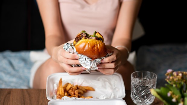 Woman eating fast food meal of burger and fries delivered at home alone
