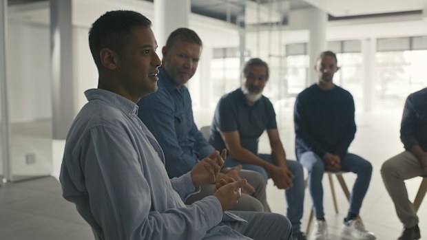Man in a group therapy meeting opening up about struggle. Community gather around and listen to therapist discuss coping mechanisms in a social support session
