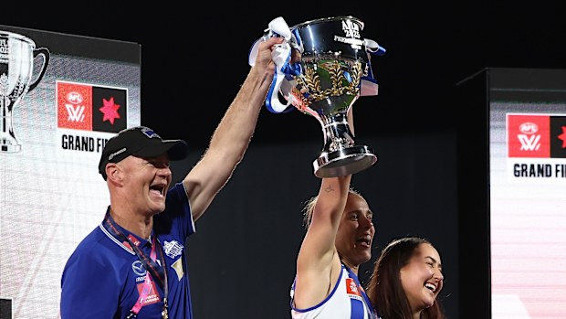 Darren Crocker, Jasmine Garner and Nicole Bresnehan of the Kangaroos lift the premiership cup