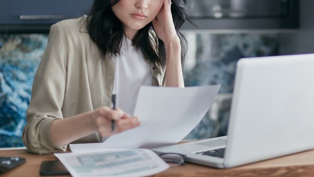 A woman looks worried about money while paying bills on a laptop. Stock photo.