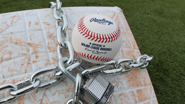 An official MLB baseball sits on top of an MLB game-used base with a lock and chain around it to represent the lockout between Major League Baseball (MLB) and the Major League Baseball Players Association (MLBPA).