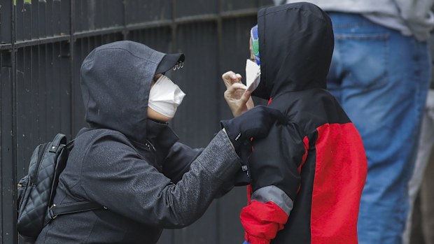 A woman adjusts her child's protective mask as they wait in line to be screened for COVID-19 at Gotham Health East New York, Thursday, April 23, 2020, in the Brooklyn borough of New York.