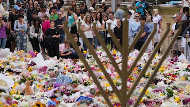 A Hanukkah menorah stands by a floral tribute as people gather to pay their respects near the Bondi Pavilion at Bondi Beach today.