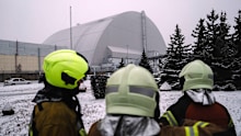 Emergency personnel watch as people inspect the damage to the radiation containment shield of Reactor Number 4 at the Chernobyl site following a February 14 drone strike.