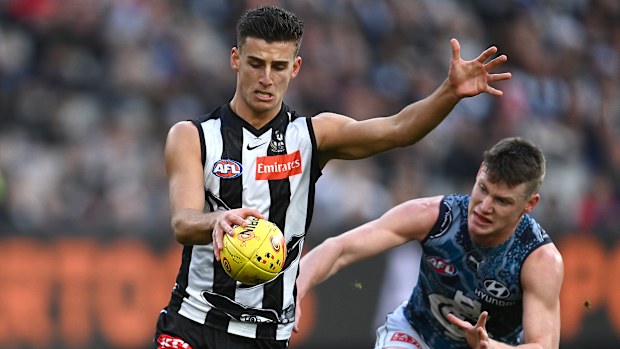 Nick Daicos kicks whilst being tackled by rival Sam Walsh.