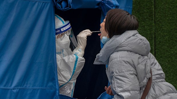 BEIJING, CHINA - MARCH 25: A health worker wears a  protective suit as she performs a nucleic acid test to detect COVID-19 at a testing site in the street on March 25, 2022 in Beijing, China. China has stepped up efforts to control a recent surge in coronavirus cases across the country, locking down the entire province of Jilin and the city of Shenyang and putting others like Shenzhen and Shanghai under restrictions. Local authorities across the country are mass testing as China tries to maintai