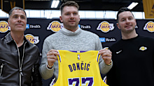 EL SEGUNDO, CALIFORNIA - FEBRUARY 04: Luka Doncic (C) of the Los Angeles Lakers holds his new jersey while standing alongside general manager Rob Pelinka (L) and head coach JJ Redick (R) during a press conference at UCLA Health Training Center on February 04, 2025 in El Segundo, California. (Photo by Harry How/Getty Images)