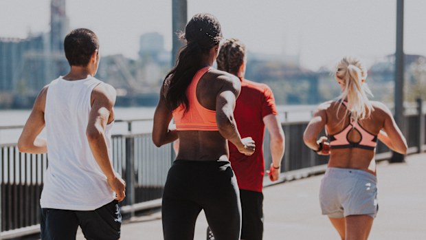A biracial group of young adult athletes participating in a group workout, jogging down a city pathway on the Willamette River in Portland, Oregon.