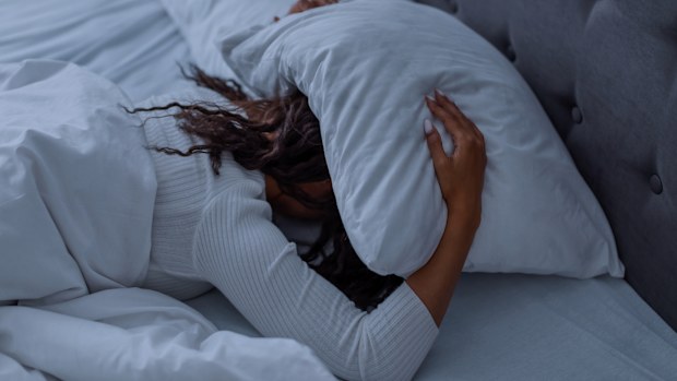 Sleeping Problem. Stressed African American lady lying alone in bed covering head under pillow feeling afraid or depressed, suffering from insomnia or mental problems after breakup