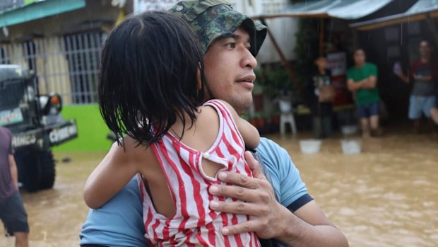A rescuer carries a child to safer grounds as floods rose due to Tropical Storm Nalgae at Parang, Maguindanao province, southern Philippines on Friday Oct. 28, 2022. (Philippine Coast Guard via AP)