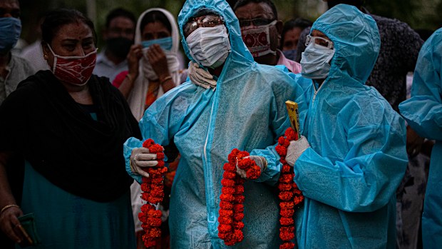 Relatives assist an Indian woman in personal protective equipment offer marigold garlands on the body of her husband  who died of COVID-19 in Gauhati, India, 