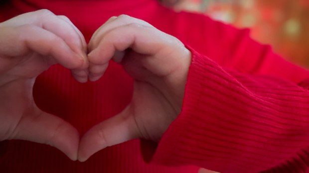 Closeup of person or child in red forming heart with hands with Christmas lights in background, charity and love concept.