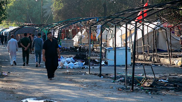 People walk amid burned tents outside the heavily fortified Green Zone in Baghdad, Iraq.