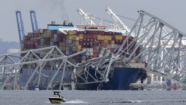 A boat moves past a container ship as it rests against wreckage of the Francis Scott Key Bridge on Tuesday, March 26, 2024, as seen from Pasadena, Md. 