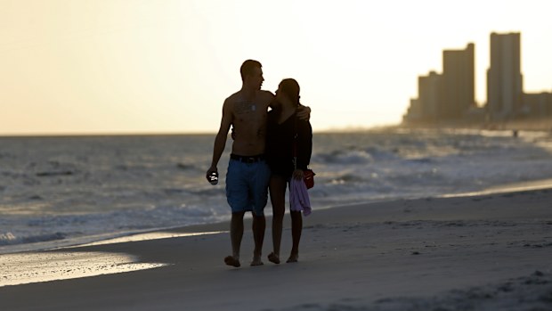 In this March 12, 2020 photo, people walk on the beach in Gulf Shores, Ala. The spring of coronavirus feels a lot like the summer of oil to residents along the Gulf Coast. Bars and restaurants are empty in Florida because of an invisible threat nearly a decade after the BP oil spill ravaged the region from the ocean floor up.