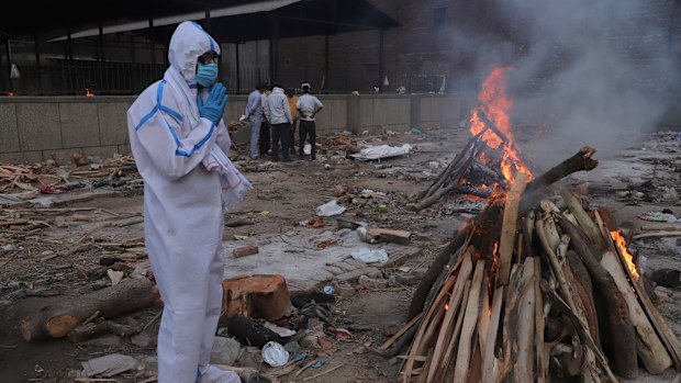 A man wearing personal protective equipment prays in front of the burning funeral pyre of his father who died of COVID-19, at a crematorium in New Delhi, India, Tuesday, May 11, 2021. (AP Photo/Amit Sharma)